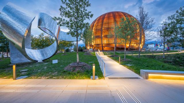 Image of a grassy area with an abstract metal sculpture on the left, and a wooden sphere on the right.