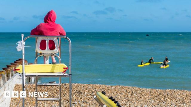 Rear view of a lifeguard sitting on a watchtower at the beach with surfers in the distance.