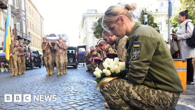Kneeling Ukrainian soldiers mourn a comrade killed in Russia's full-scale invasion