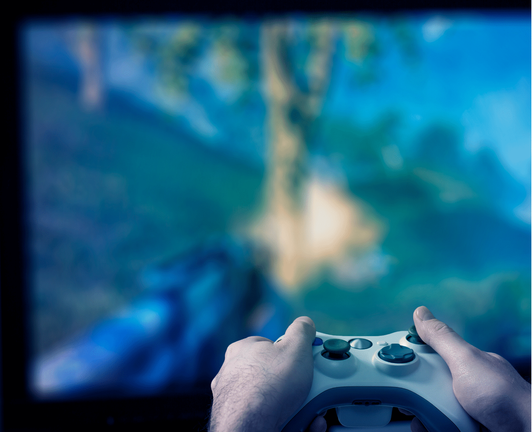 A wider shot showing both hands gripping a white video game controller, focused on a television screen with a blue-green blurred gaming scene in the background. A wider shot showing both hands gripping a white video game controller, focused on a television screen with a blue-green blurred gaming scene in the background.
