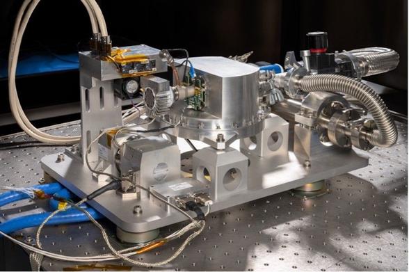 complex metal device with various protruding tubes and wires sits on a metallic work surface