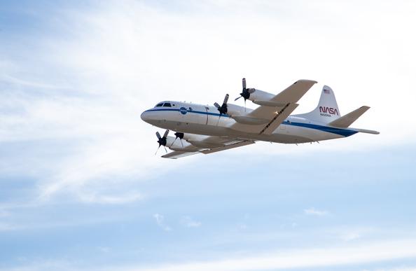 An aircraft with four propellers and NASA logos on the side is airborne and surrounded by blue sky.