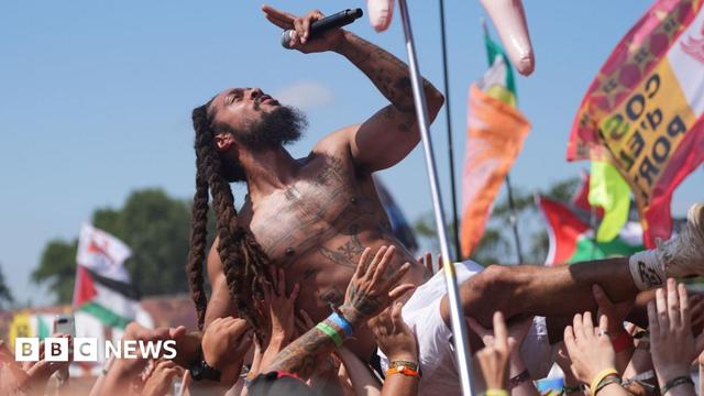 A performer with long dreadlocks sings into a microphone while crowd surfing.