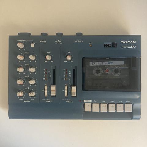 Portastudio Tascam Porta 02. Es un equipo de grabación multipistas con cassette. Es azul, a la izquierda se ven los potenciómetros para los ajustes y a la derecha la ranura para el cassette y los controles de play, rewind, stop...