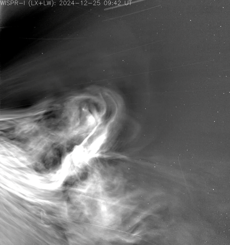 A grayscale space image shows bright, swirling solar plasma or coronal activity against a dark background, with faint stars visible and thin streaks crossing the scene. The top displays the label "WISPR-I (LX+LW): 2024-12-25 09:42 UT.
