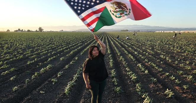 CAMARILLO, CALIFORNIA - JULY 10: Community member Ana waves an American-Mexican flag in a show of support for detainees near federal agents blocking protestors during an ICE immigration raid at a nearby licensed cannabis farm on July 10, 2025 near Camarillo, California. Ana said she knows some of those detained and their families. Protestors stood off with federal agents for hours outside the farm in the farmworker community in Ventura County. A Los Angeles federal judge is set to rule Friday on a temporary restraining order which would restrict area immigration enforcement operations. (Photo by Mario Tama/Getty Images)