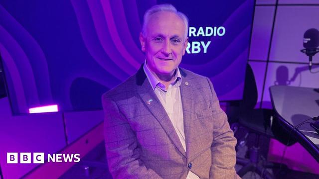 Man in brown tweed jacket with short grey hair sat in radio studio infront of purple background with BBC Radio Derby logo on 