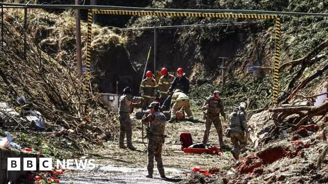 Uniformed officers search the site of the explosion in Quatro Barras, Brazil. Debris, including tree trunks and branches, can be seen scattered across the site. Some officers carry shovels.