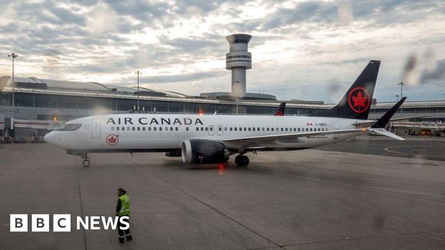 An Air Canada aircraft sits on a runway with an air traffic control tower in the background.