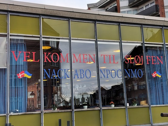 A window with the Danish words “VELLOMMEN TIL SLØJFEN” (“Welcome to the loop/bowtie”) and the faux Cyrillic words “NACKABO NPOCNMO”, which are an attempt at writing the Ukrainian phrase “Ласкаво просимо” (“Welcome” or “Please come in”)