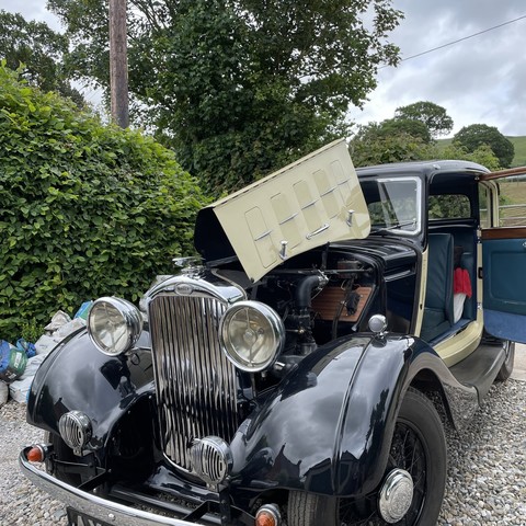 a vintage Humber car, black and cream coloured. Its bonnet is open on the near-side, its engine visible. The single passenger-side door is also wide open, revealing the blue leather seats