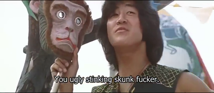 Image from the 1982 martial arts film 'Ninja in the Dragon's Den', directed by Corey Yuen. It shows Conan Lee holding a monkey mask and saying to someone off-camera, 'You ugly stinking skunk fucker.'