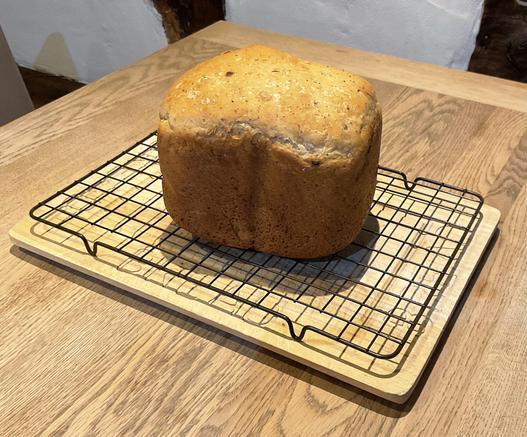 a freshly baked loaf of bread- dark crust, well risen, standing on a wire rack and wooden bread board on an oak table too