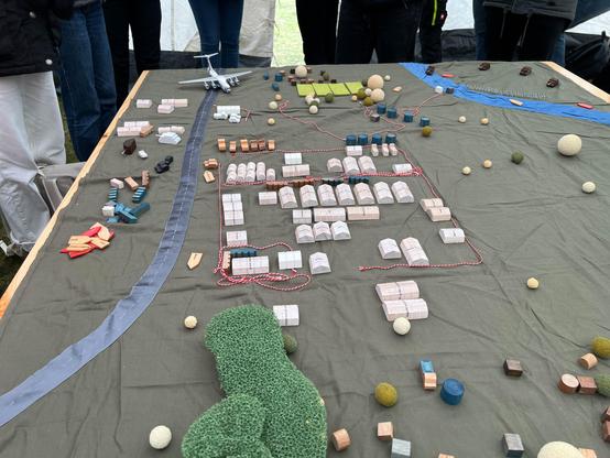 Tabletop Planspiel zum Camp Management der Emergency Response Unit Hospital der Deutschen Roten Kreuzes - Auf dem Tisch ist eine Miniaturversion des aufgebauten Krankenhauses neben einem Flüchtlingslager zu sehen.