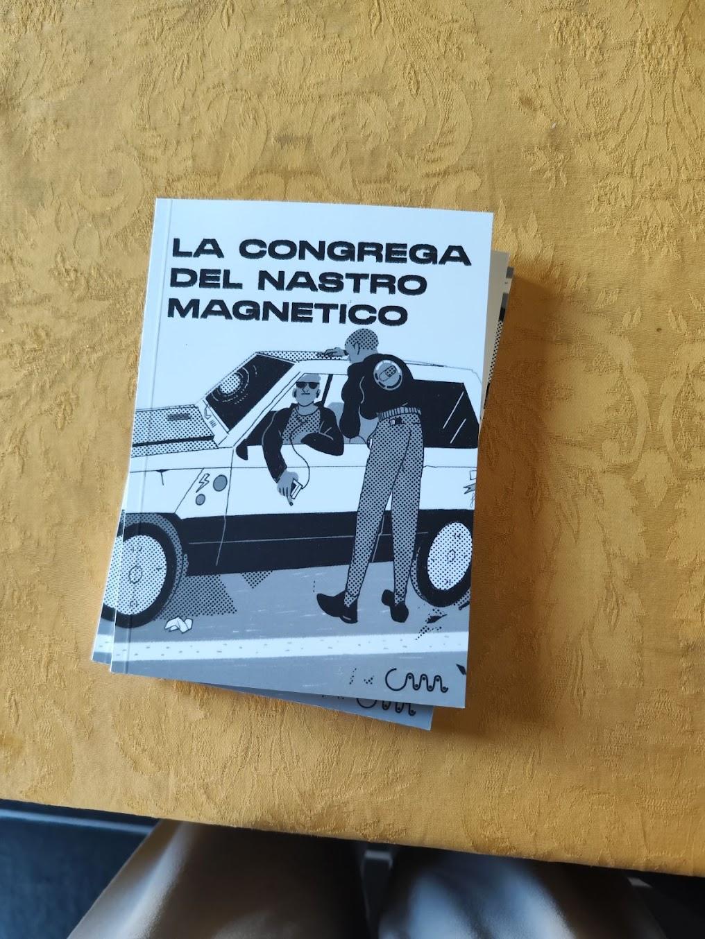 Prime copie di LA CONGREGA DEL NASTRO MAGNETICO, su una tovaglia gialla. In copertina c'è uno scambio di cassetta tra un uomo su una panda e un altro in piedi.