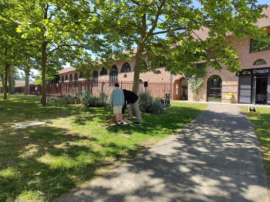 Deux jeunes constatants les résultats d'un jeu de lancer, des arbres et un bâtiment industriel en arrière fond