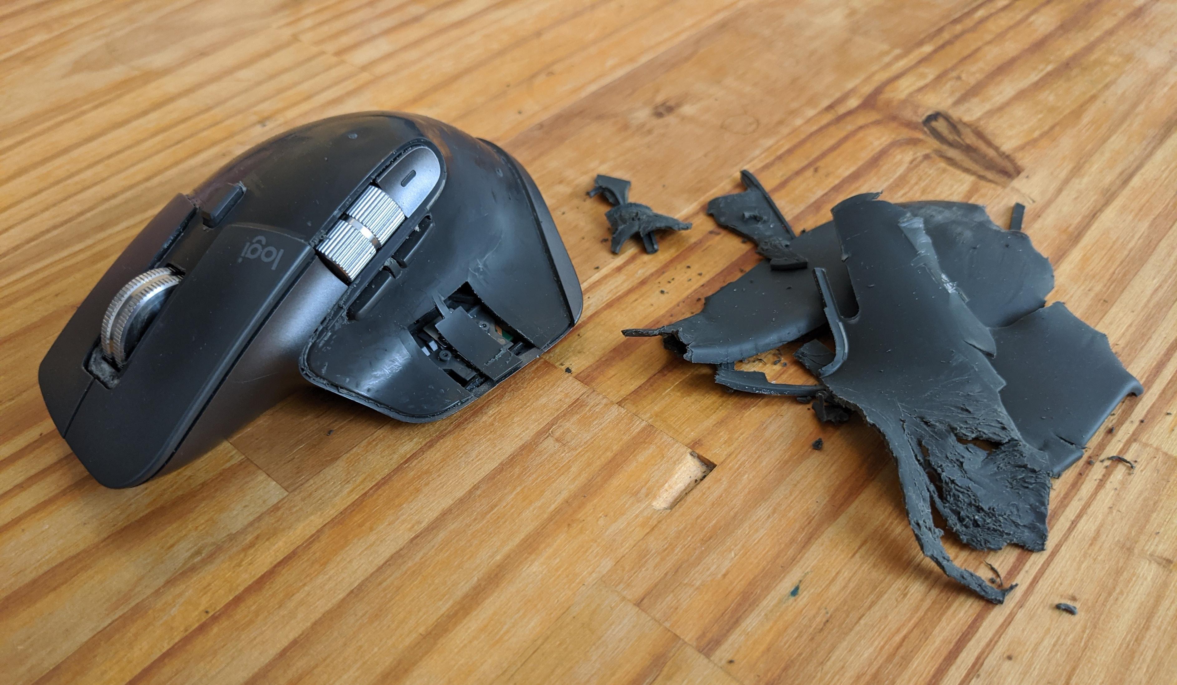 A photo of a Logitech MX Master mouse, with the rubber coating removed, torn off, and lying next to it on a wooden table.