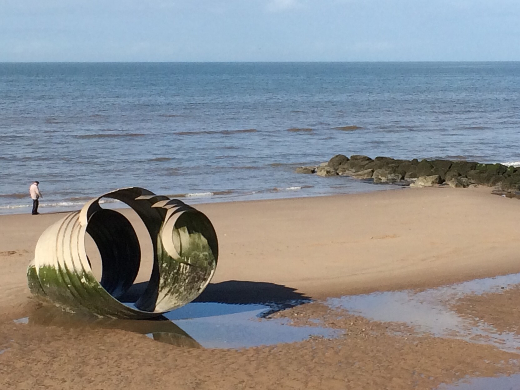 A large metallic conical sea-shell sculpture sat on a beach.  The sculpture is about 10 metres from the waterline. Part of the stone sea defences can be seen to the right, jutting out to the sea.  

The sculpture was made as part of The Mythic Coast project (conceived by Stephen Broadbent) which is linked to the ongoing sea defence works in Cleveleys.