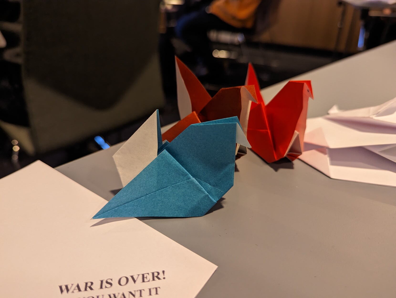 Three differently colored origami hens sitting on a great table.