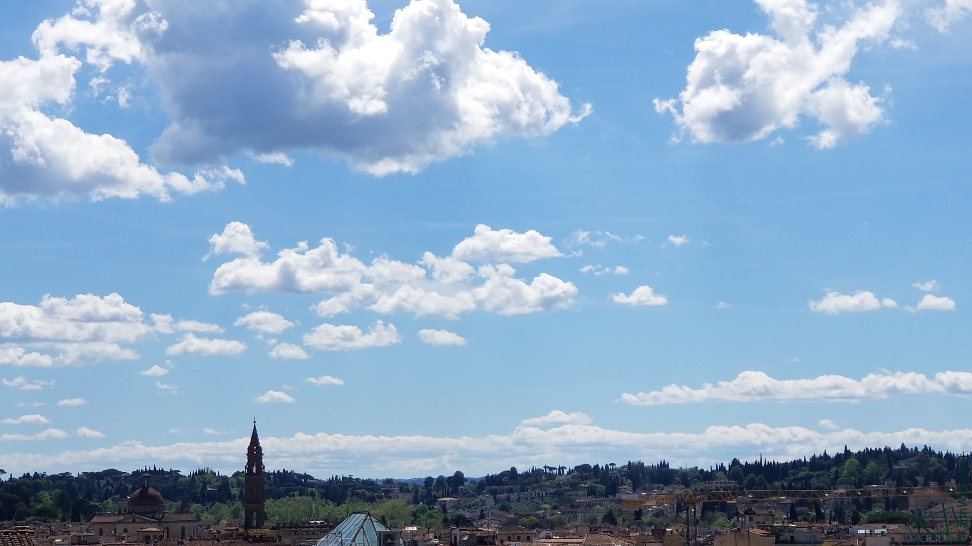 Photo of gorgeous fluffy clouds drifting through a light blue sky over Florence Italy.