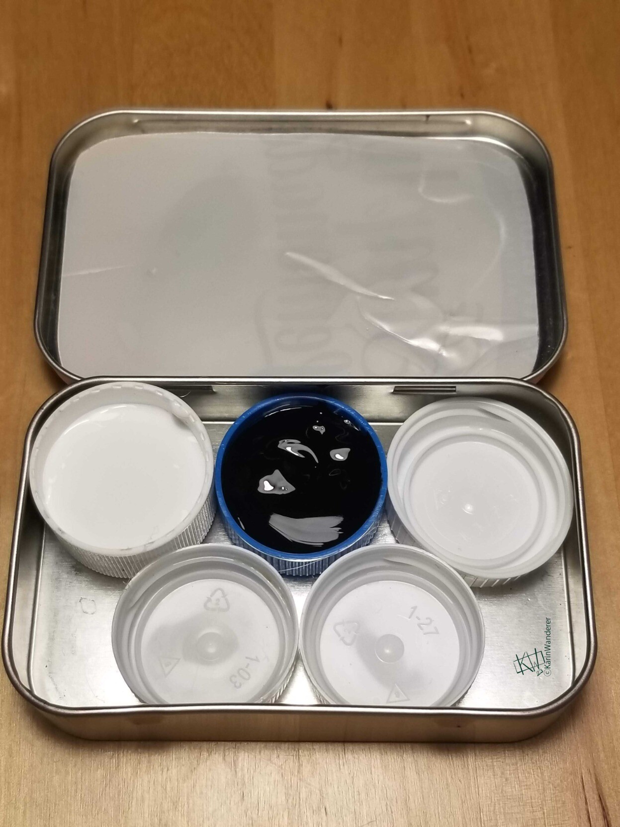 5 Bottle caps are inside a small lidded tin. 2 have paint in them- black & white.  An oblong piece of thin plastic is glued inside the lid of the tin.