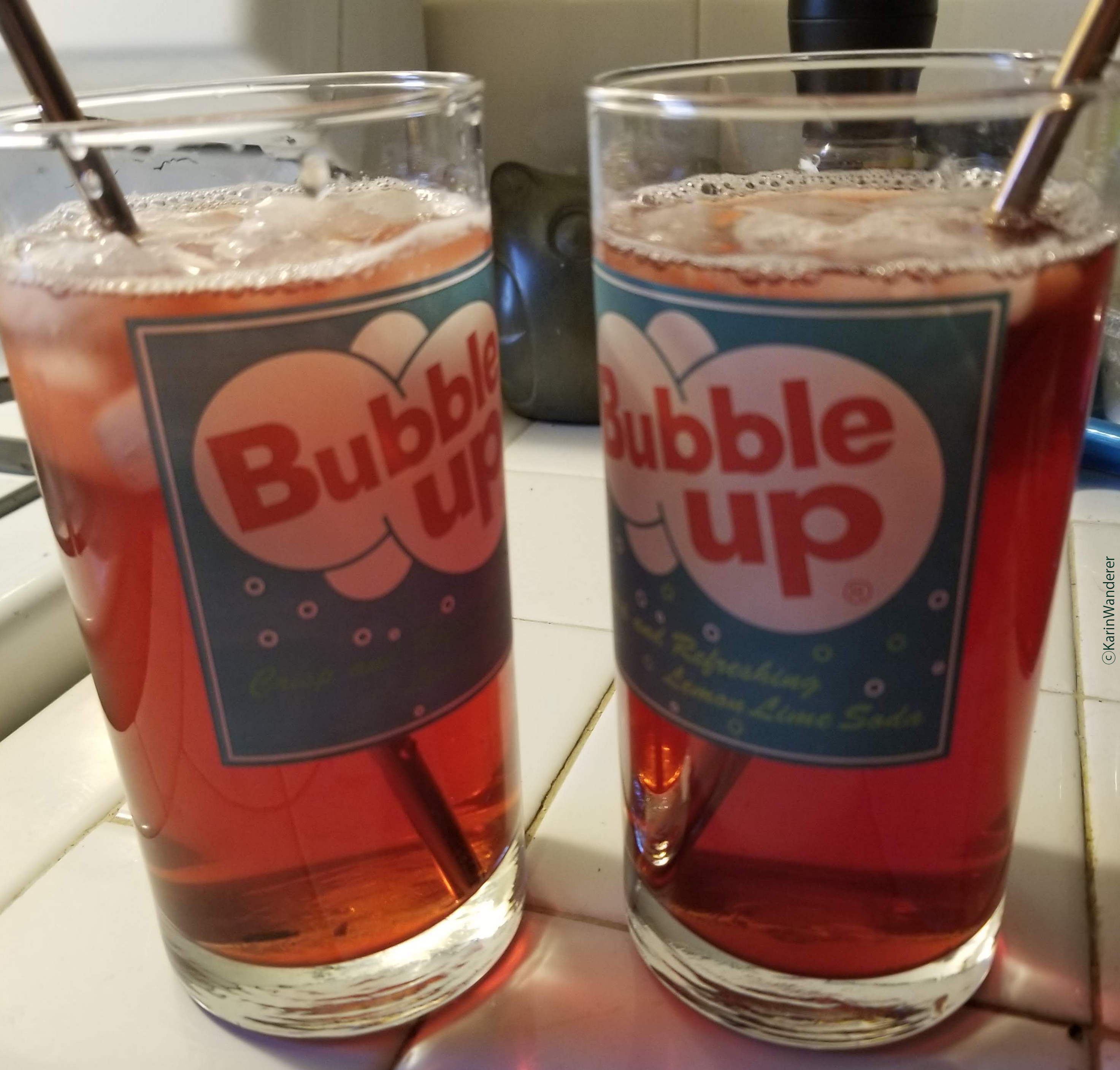 Two glasses full of iced tea sit on a counter. The glasses say "Bubble Up" & have straws sticking out of them.