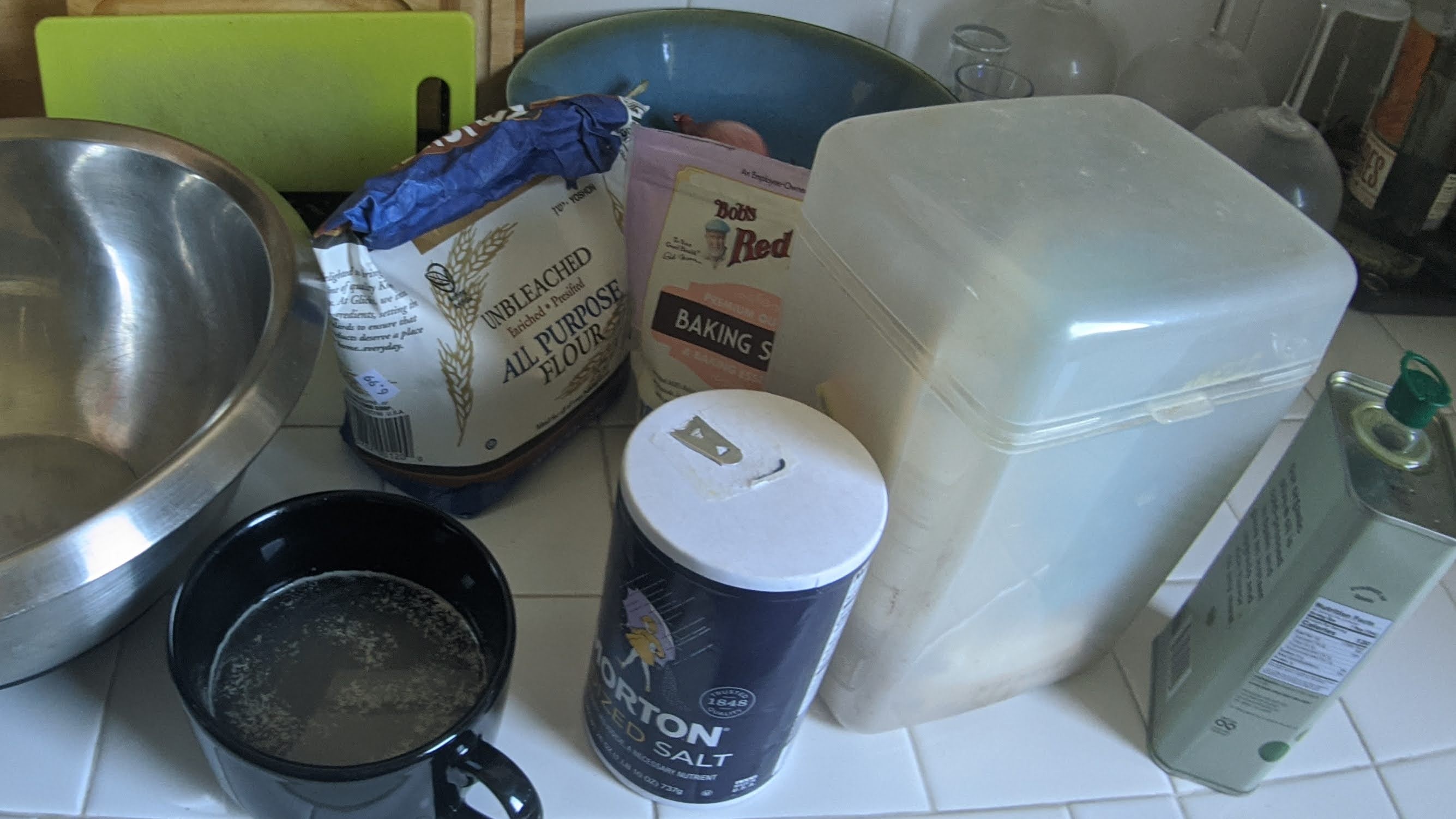 Kitchen counter is crowded with a mixing bowl & ingredients, such as salt. flour, & baking soda.