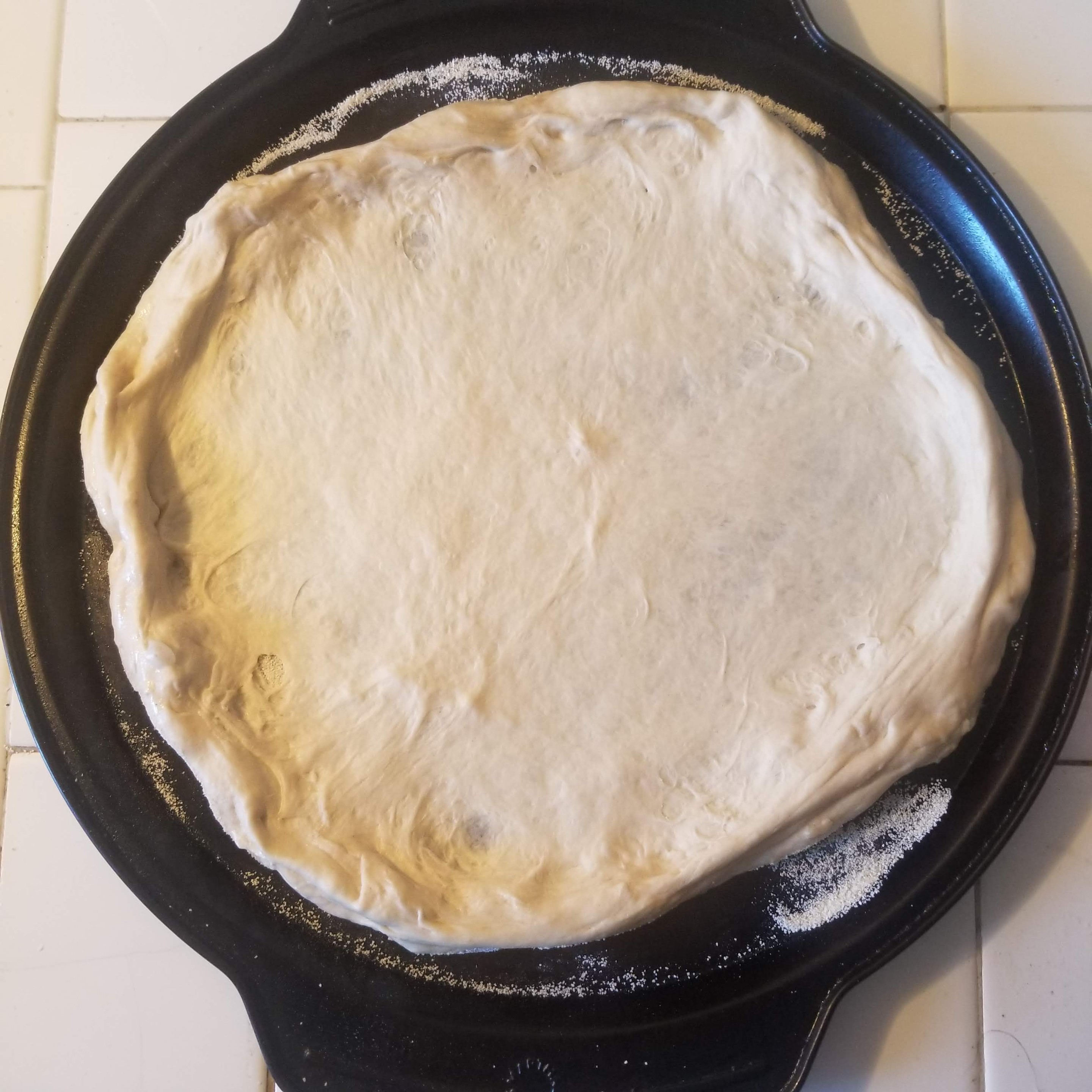 A round baking pan with a raw pizza crust on it.