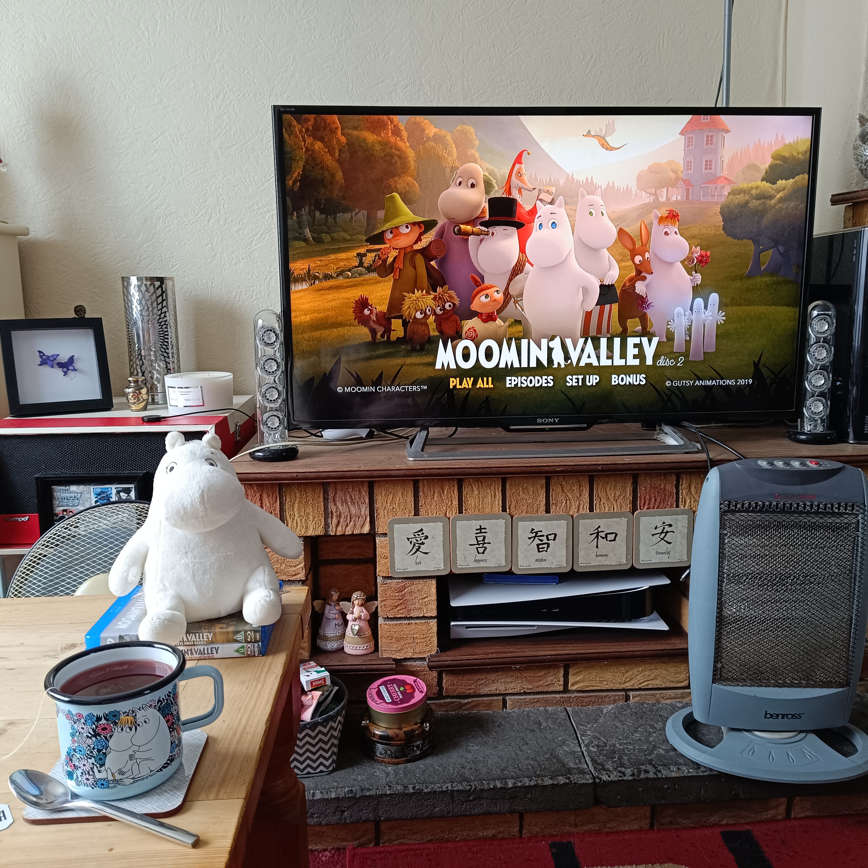 Photo of my TV showing Moominalley on Blu-ray, and nearby is a coffee table with a Moomin enamel mug, A Moomin plushie and two boxes of Moominvalley on Blu-ray.