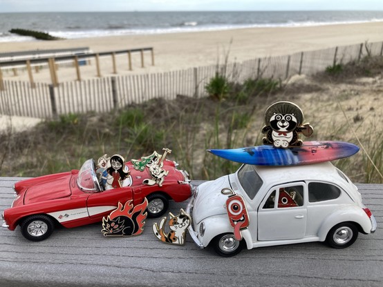 a model convertible and old VW bug with a surfboard on the roof and a bunch of yokai pins riding in and hanging out around them