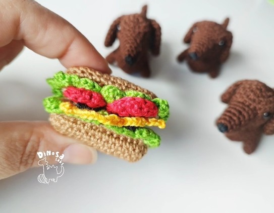 Sandwich de amigurumi estilo perrito caliente (diseño dinosalabs). Al fondo se ven 3 perritos salchicha de amigurumi (diseño canal crochet)
