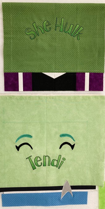 Two green minimalist quilt blocks, one that represents Tendi with a section at the bottom that resembles her medical blue uniform and her happy eyebrows above. The other represents She Hulk with a pieced section below that resembles her purple, white and black super suit