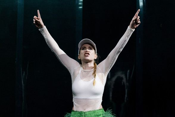 Szenenfoto mit Sina Martens in einem weißen Netzoberteil mit Cap und erhobenen Armen nach oben zeigend