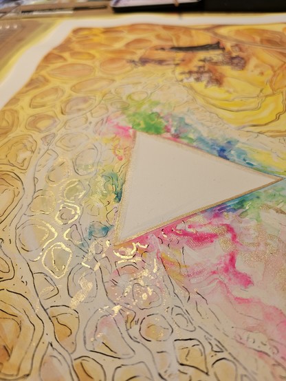 Angled shot of the triangle with colours coming out of it, and some gold paint shimmers