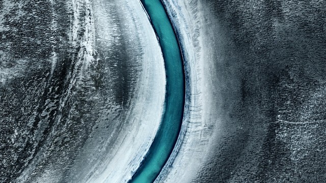 a blue river going through a black and white wintery landscape, seen from above