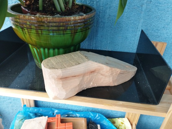 A piece of wood carved into a vaguely foot shape. It is under a flower pot.
