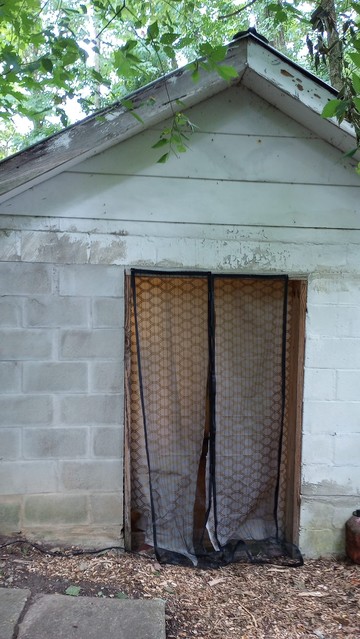 Outside view of the small cinder block building with metal roof that I've converted into my studio. There's no door, so I've covered it with a self-closing mosquito net on the outside and shower curtain on the inside.