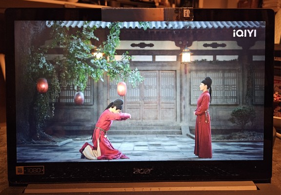 Li Bing kneeling in his paved inner yard, wearing red officials' clothes. He's under a tree where someone has hung three red lanterns, and in front of hom stands another official in red robes, ready to give an oral decree.