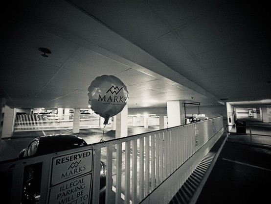 Black and white photo of a forlorn ballon tied to a railing in an empty parking garage