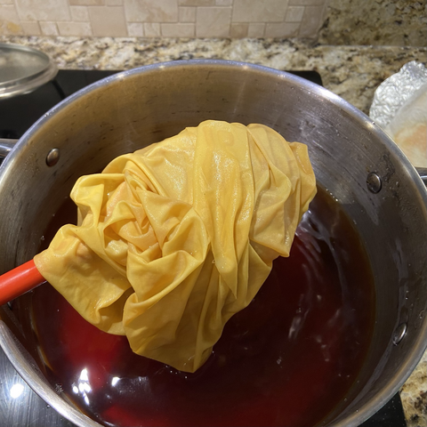 Golden buttery dyed cotton fabric being lifted out of the dye pot with a spoon 