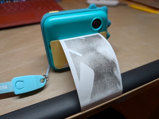 Children toy camera with a built-in thermal printer. The camera looks like a Dinosaur, and the print is coming out of its mouth. The print is awful, it doesn't look like anything. 