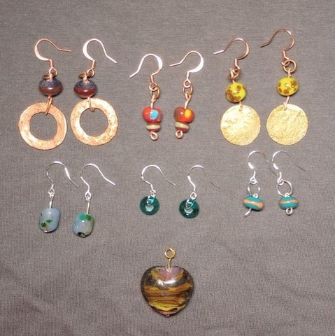 Photo of the first few new pieces I've made in 6 weeks due to moving, including 6 pair of earrings in copper and silver with my handmade glass beads, and a heart pendant made in various warm shades of transparent glass.