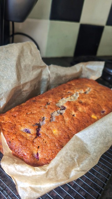 a large banana bread containing additional chocolate chips and home grown raspberries. its still wrapped in parchment and sat on a cooling rack