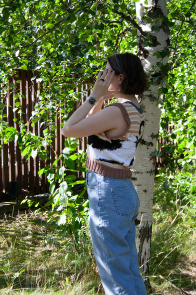 Woman in a knitted vest standing side to the camera, the side of the picture is visible, so the cat wraps around the vest