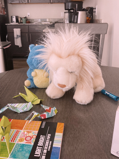 A photo of a plush lion and origami crickets sitting on a kitchen table. 