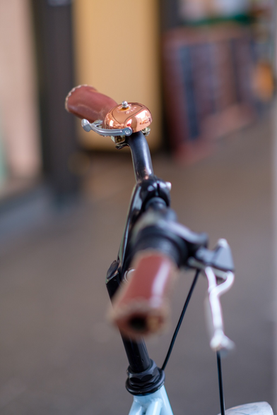 Ein Fahrradlenker mit Kupferfarbener Klingel. 