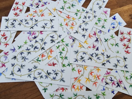 A view of scattered hand-painted bookmarks on a wooden table. The bookmarks have colourful maple leaves on a golden stem.