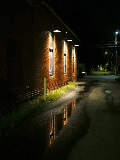 A nighttime photo of three lights illuminating an old brick wall with windows in a dark alley