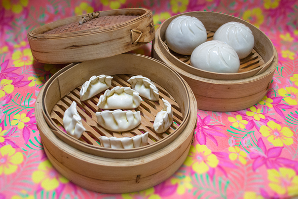 Ceramic gyoza and siopao, arranged in a bamboo steamer. This is all displayed on a pink tropical floral cloth