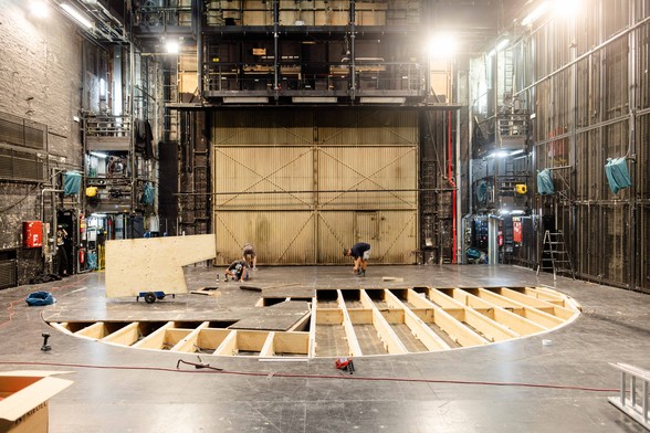 Personen arbeiten auf dem Boden im Bühnenbereich des Großen Hauses, ein Bereich auf einer halbkreisrunden Fläche ist nicht mit Platten bedeckt, man sieht eine Holzkonstruktion darunter